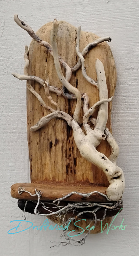 This one-of-a-kind, unique driftwood tree wall hanging with a small shelf was handmade with small white driftwood sticks collected along the Oregon Coast. To make it, the driftwood sticks are assembled one at time creating a tree and some roots that are attached to a beige flat piece of driftwood.
