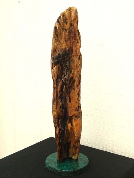 This is a driftwood branch that is dark yellow and black in color that is mounted to a round, hand painted green and black base and varnished to protect the driftwood