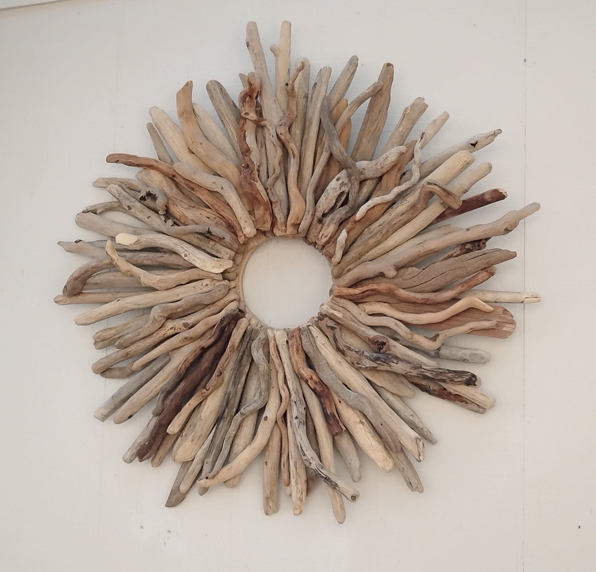 This large naturally weathered driftwood wreath adds a touch of organic elegance to any home. Handcrafted from real driftwood, the starburst design creates a unique and eye-catching focal point. Perfect for rustic or coastal decor, this wreath is a must-have for nature lovers.